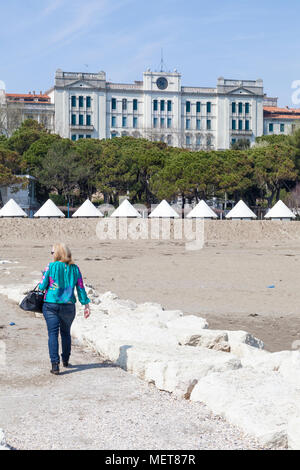 Ancien luxueux Grand Hotel des Bains, Lido di Venezia, Venise, Vénétie, Italie Vue d'un brise-lames sur la plage avec une femme marche arrière le long de c Banque D'Images