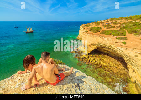Benagil, Portugal - 23 août 2017 : le mode de vie de couple en vacances d'été, les bains de soleil sur les falaises en côte de l'Algarve, célèbre pour ses formations rocheuses. Benagil grotte, une grotte marine populaire sur la falaise en face. Banque D'Images