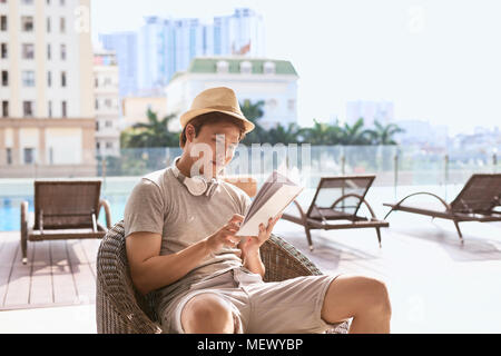 Young Asian man reading book de la piscine sur un jour d'été ensoleillé Banque D'Images