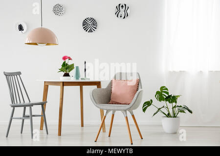 Fauteuil gris avec coussin rose à côté d'une table en bois et une chaise de salle à manger moderne avec des intérieurs Banque D'Images