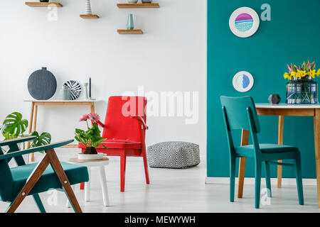 Fauteuil rouge et bleu à table avec des fleurs dans le salon intérieur avec des plaques sur un mur vert Banque D'Images