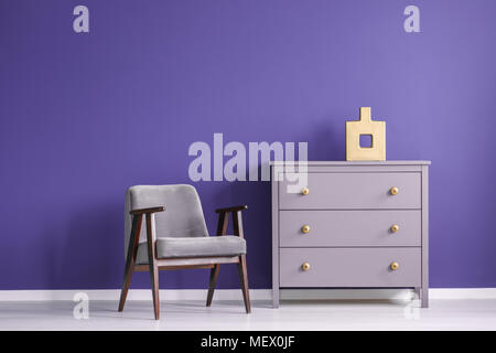 Fauteuil en bois gris à côté d'un mur violet violet contre l'armoire à l'intérieur salle de séjour minimal Banque D'Images