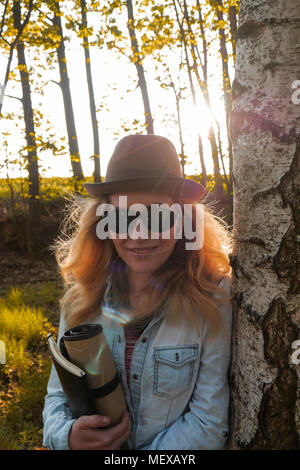 Young caucasian woman artiste portant un chapeau élégant, debout dans une forêt de bouleaux tenant son portable Banque D'Images