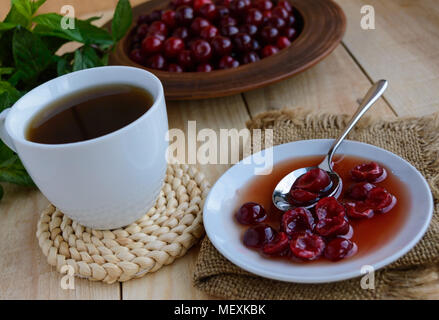 Confiture de cerise et d'une tasse de thé sur un fond en bois clair. Banque D'Images