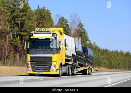 Camion Volvo FH jaune transporte trois nouveaux cars le long de la route sur un beau jour de printemps à Raasepori, Finlande - le 20 avril 2018. Banque D'Images