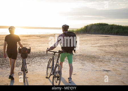 Deux jeunes hommes sur un vélos de cyclotourisme avec des sacs et casques dans le désert sur un voyage en vélo, amis'avoir in sunny day Banque D'Images