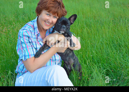 Cheerful woman, maman, femme au foyer, tenir, pet prix chien. noir, jeune bouledogue français. vieille femme ressemble à l'appareil photo. Entreprise d'été heureux sur vert Banque D'Images