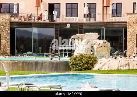 Les baigneurs se détendent dans la piscine thermale de l'hôtel Adler Thermae près de Bagno Vignoni, en Toscane, Italie, devant un rocher cascade artificiel ; sur le balcon au-dessus, d'autres invités en peignoirs observent. La famille Sanoner gère ce complexe de 90 chambres avec environ 1 000 mètres carrés de surface d'eau, alimenté par des sources chaudes à 50 degrés Celsius dans la Val d'Orcia protégée par l'UNESCO. Banque D'Images