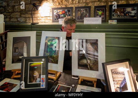 Contrôle de sa calculatrice photographe derrière ses images encadrées sur un étal de Cirencester's Hall de maïs Banque D'Images