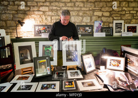 Contrôle de sa calculatrice photographe derrière ses images encadrées sur un étal de Cirencester's Hall de maïs Banque D'Images