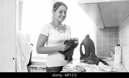 Photo en noir et blanc de smiling woman le tri des vêtements propres de la blanchisserie Banque D'Images