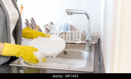Jeune femme en appliquant des gants jaune sur la vaisselle détergent suds Banque D'Images