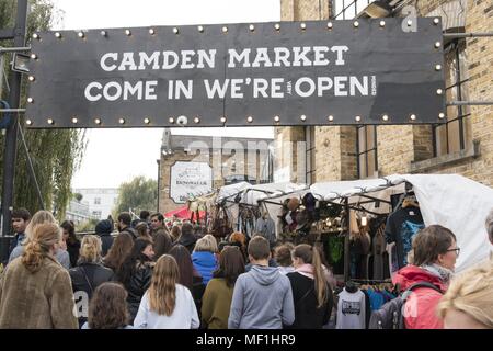 La foule d'acheteurs, de passer sous un panneau d'entrée "Marché de Camden viennent dans nous sommes (très) Ouvert (d'esprit), ' et la marche dans une rue piétonne, bordée d'étals de marché en plein air, à Camden Lock Market, situé dans le nord-ouest de Londres, Royaume-Uni, le 28 octobre 2017. () Banque D'Images