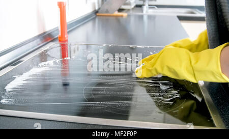 Libre de droit de jeune femme en jaune des gants en latex sur une plaque électrique nettoyage cuisine Banque D'Images