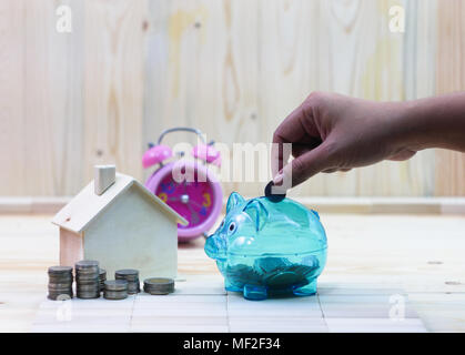 Part des femmes Déposer pièces dans une tirelire claire sur la table en bois et autour de a une maison, les pièces de monnaie pile et un réveil Banque D'Images