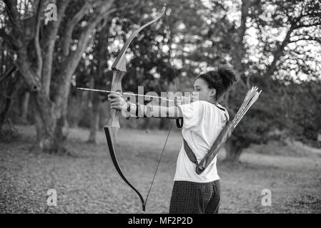 Girl visant un arc et une flèche dans la forêt Banque D'Images