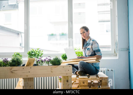 Remise à neuf femme sa nouvelle maison avec des palettes, using laptop Banque D'Images