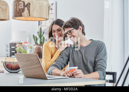 Couple heureux avec un ordinateur portable à l'aide de cartes sur table à la maison Banque D'Images