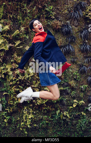 Portrait de jeune femme à la mode dans l'air de saut en avant du Mur vivant Banque D'Images