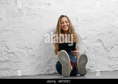 Riant Portrait jeune femme assise sur le sol à l'aide de tablet Banque D'Images