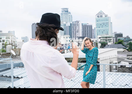 Homme TYoung avec smartphone prendre photo de copine posing on rooftop Banque D'Images
