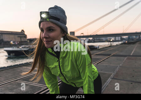 Jeune femme sportive avec projecteur au crépuscule au bord de la rivière dans la ville Banque D'Images