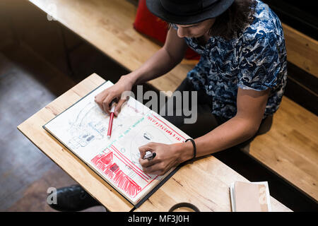 Artiste assis dans un café, dans son carnet de dessin Banque D'Images