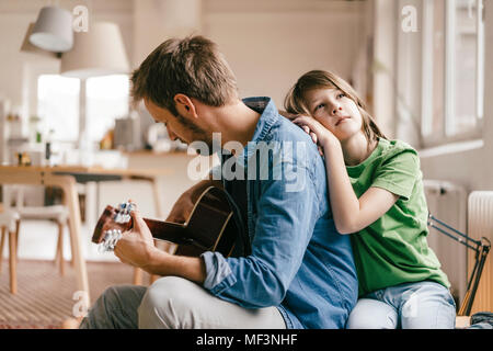 Appuyé contre son père jouer de la guitare à la maison Banque D'Images