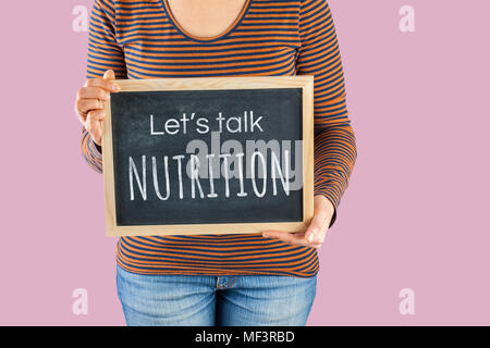 Les mains tenant petit tableau noir à l'avant du corps avec un texte disant parlons Nutrition Banque D'Images