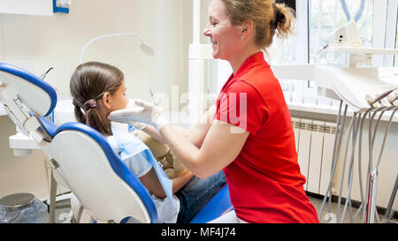 Le dentiste pédiatrique à sourire à son patient assis dans la chaise du dentiste Banque D'Images