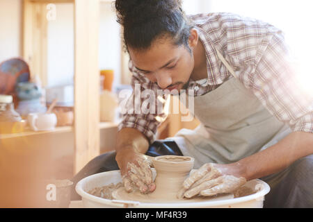 Portrait of young handsome mixed race male potter faire vase d'argile sur la poterie dans l'atelier de la roue tourne Banque D'Images