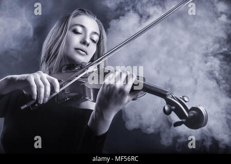 Image en noir et blanc. Belle Jeune femme jouant du violon. Le brouillard à l'arrière-plan. Studio shot Banque D'Images