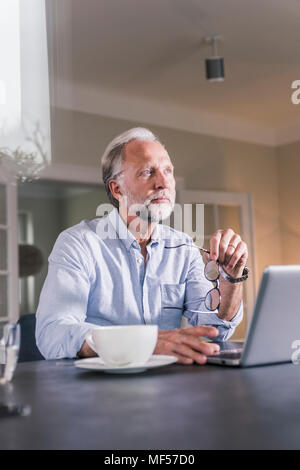 Portrait of smiling man sitting at table with laptop à distance à Banque D'Images