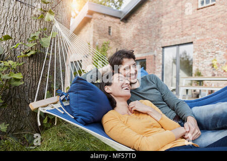 Heureux couple couché dans un hamac dans le jardin de leur maison Banque D'Images