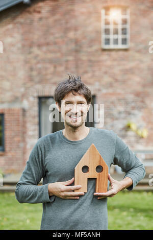 Portrait of smiling man devant sa maison holding house model Banque D'Images