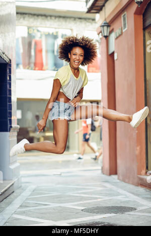 Espagne, Andalousie, Malaga. Happy black woman, afro hairstyle jumping in urban street portant des vêtements décontractés. Vie de la jeunesse urbaine. Banque D'Images