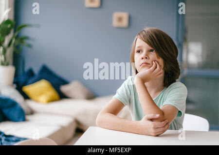 Portrait de sad boy sitting at table at home Banque D'Images