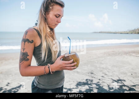 Cuba, jeune femme avec tattoo à Playa de miel de boire l'eau de noix de coco Banque D'Images