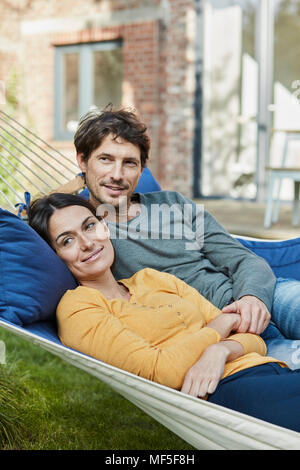 Smiling couple couché dans un hamac dans le jardin de leur maison Banque D'Images