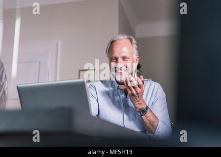 Portrait of smiling young man using laptop and cell phone at home Banque D'Images