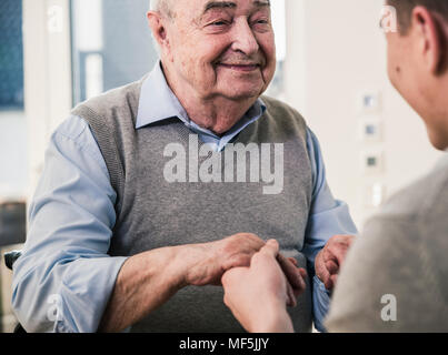 Senior man smiling at young man holding ses mains Banque D'Images