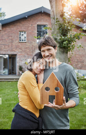 Portrait of smiling couple dans le jardin de leur accueil holding house model Banque D'Images