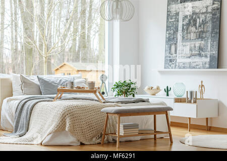 Peinture au-dessus de l'armoire blanche dans l'intérieur chambre à coucher moderne gris avec banc en face du lit Banque D'Images