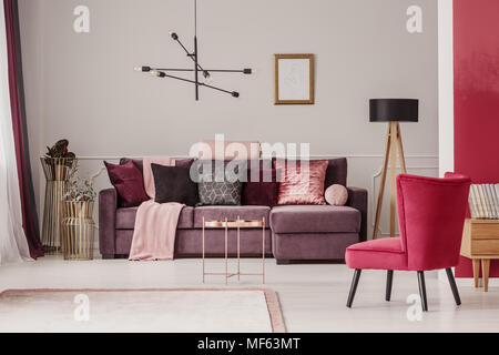 Table de cuivre près de violet canapé d'angle et fauteuil rouge à l'élégant salon intérieur avec immersive Banque D'Images