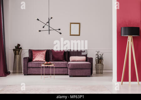 Lampe en bois contre le mur rouge dans un salon avec canapé d'angle intérieur violet Banque D'Images