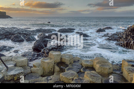 Giant's Causeway, l'Irlande du Nord, au Royaume-Uni pendant les hivers. Les vagues féroces de l'emblématique pâte côte de l'Irlande du Nord. Dans une distance le ciel s'allume avec s Banque D'Images