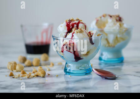 Crème glacée à la vanille dans un bol bleu,sur fond blanc,vue latérale,écrous et berry sirop sur la crème glacée. Banque D'Images