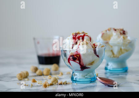 Crème glacée à la vanille dans un bol bleu,sur fond blanc,vue latérale,écrous et berry sirop sur la crème glacée. Banque D'Images