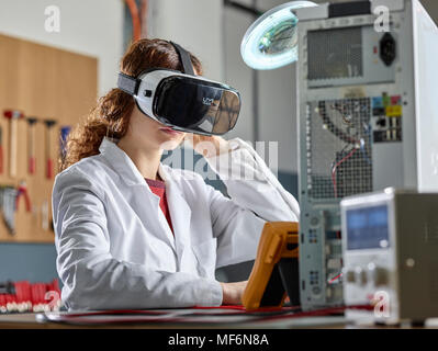 Femme avec des lunettes de VR et manteau de laboratoire assis en face de l'ordinateur n'est ouvert dans un laboratoire électronique, Autriche Banque D'Images