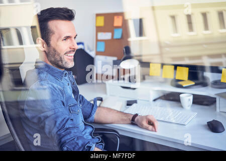 Smiling man looking through window in office sitting at desk Banque D'Images